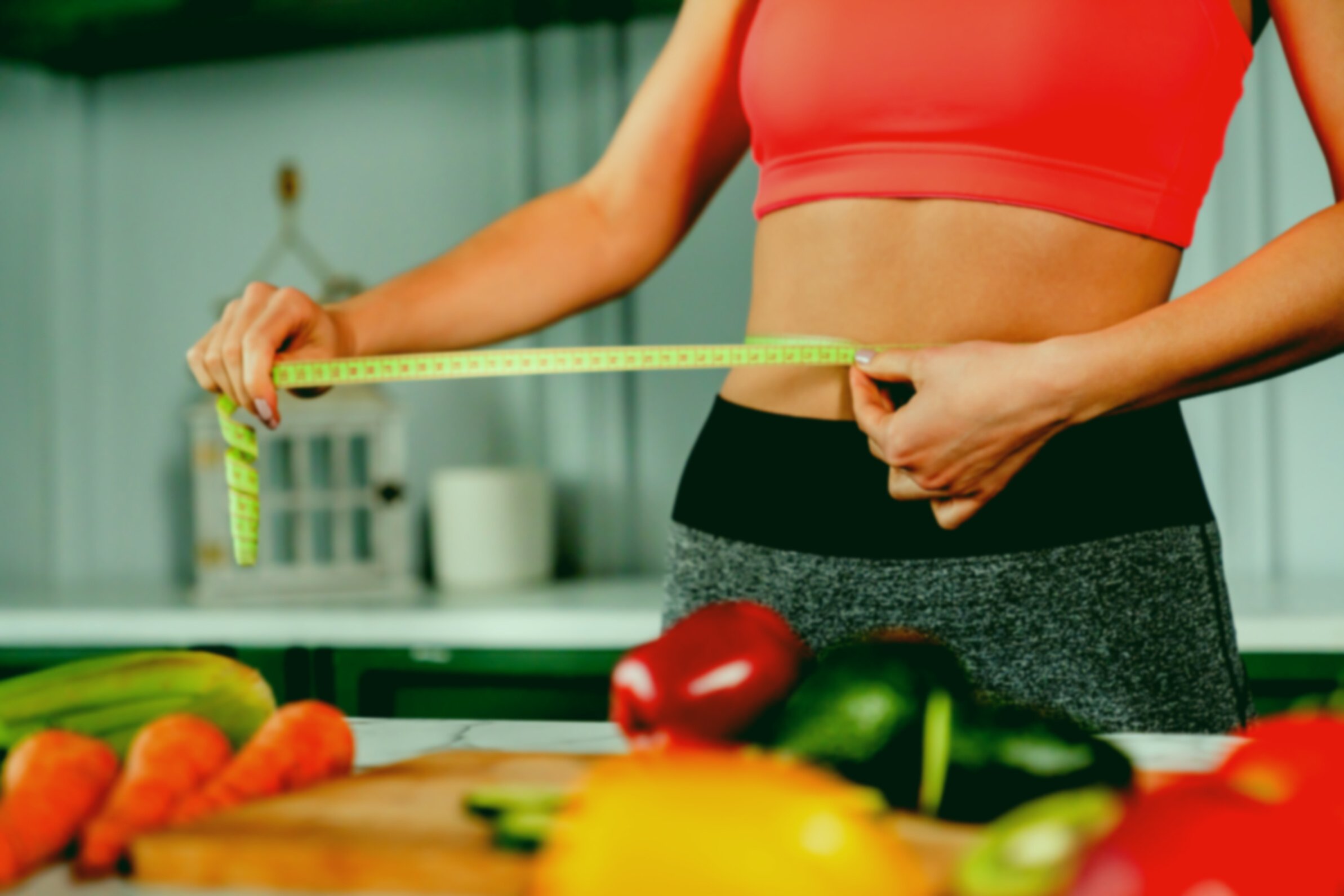 Healthy fit girl measuring her waist with measuring tape in the kitchen